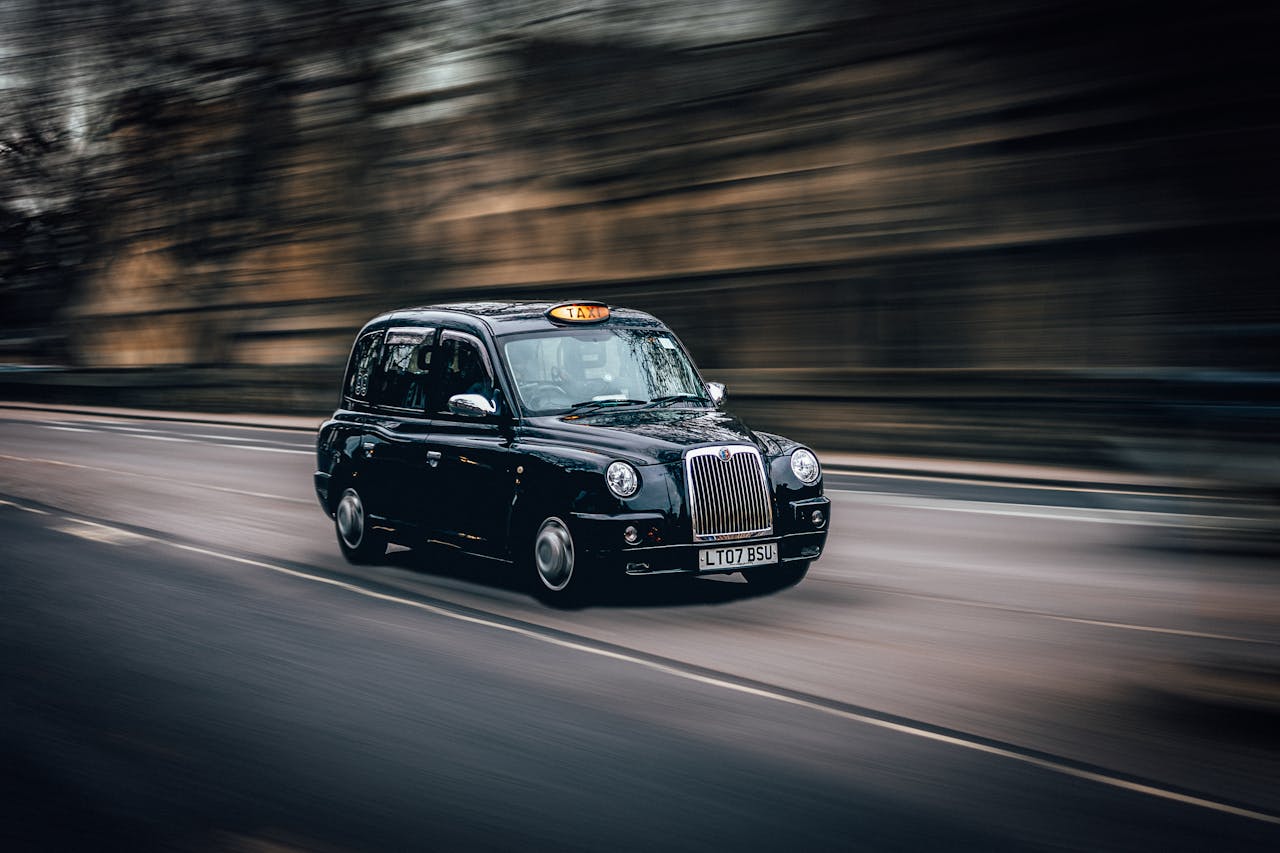 our-experience A black London taxi rapidly cruises down a street in Oxford, capturing the essence of classic British transportation.