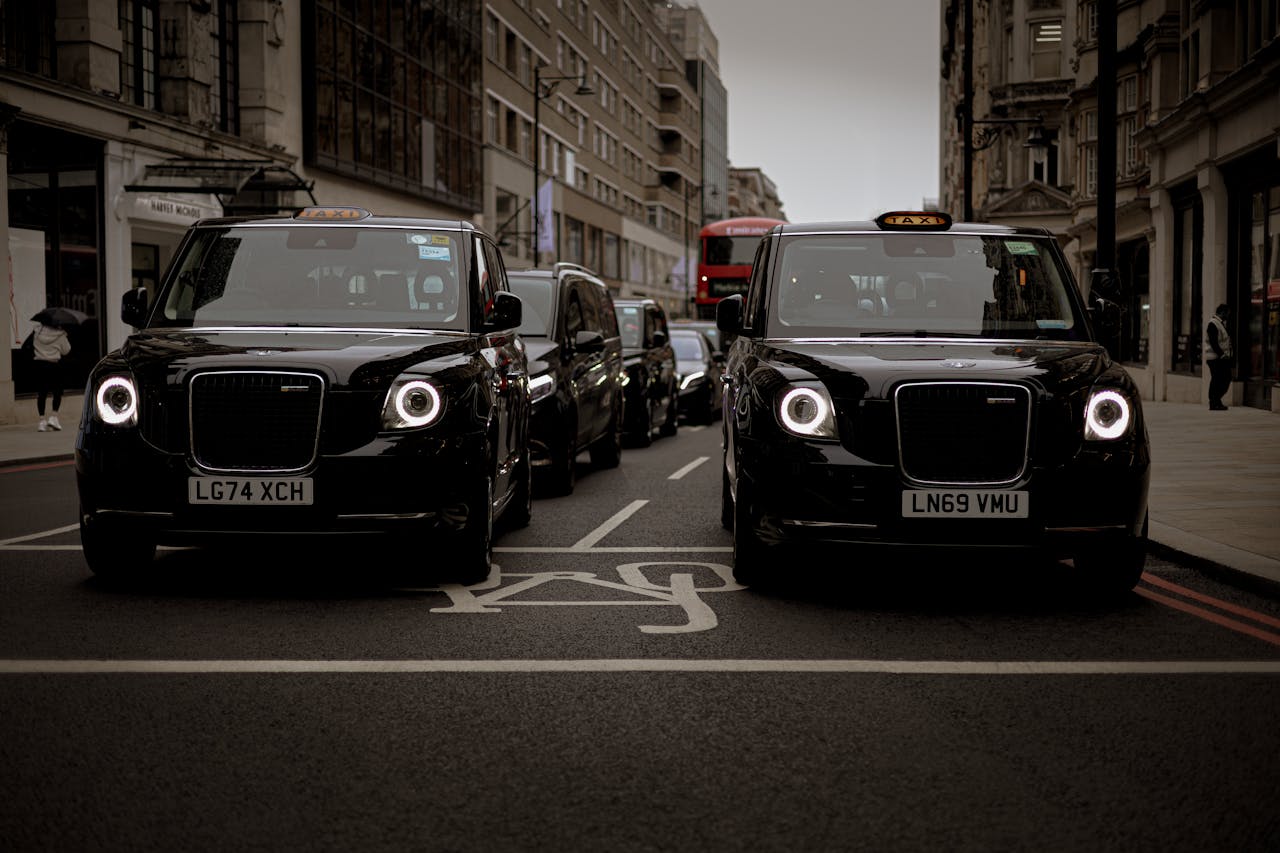 about-img Black taxis line up on a London street showcasing modern urban transportation.