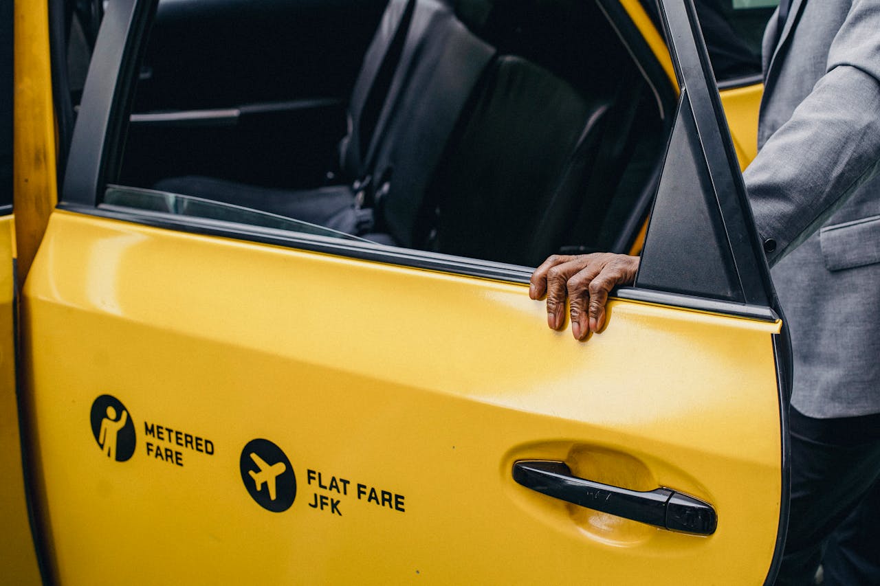 services-img A person opens a yellow taxi door with JFK flat fare signage.