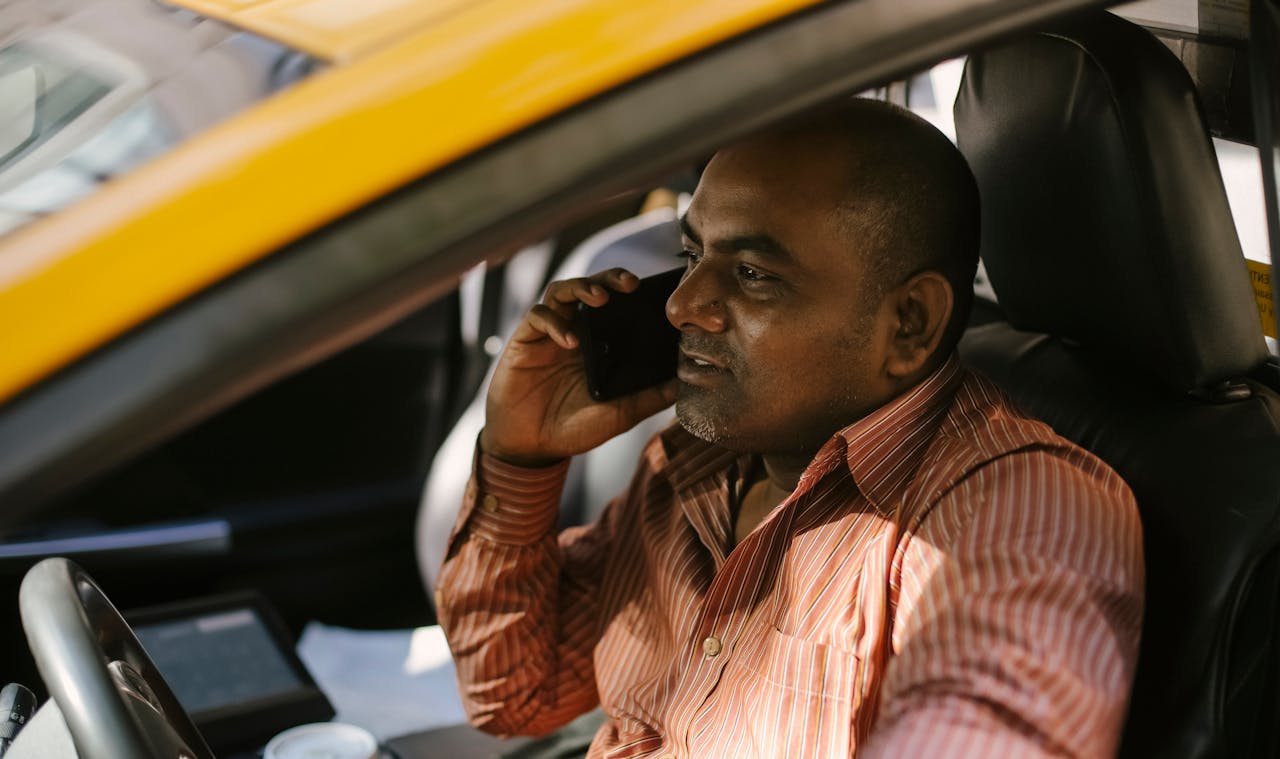 services-02 Ethnic male cab driver in striped shirt talking on cellphone in transport while looking away